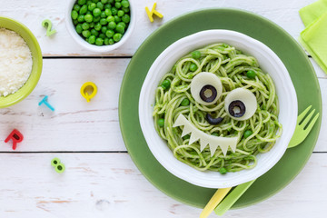 Fun food for kids - cute smiling face of green spaghetti monster served in a white bowl with eyes...