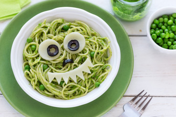 Fun food for kids - cute smiling face of green spaghetti monster served in a white bowl with eyes...
