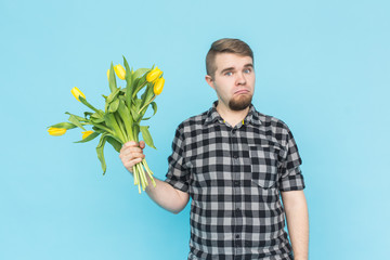 Caucasian handsome man with bunch of yellow tulips on blue background.