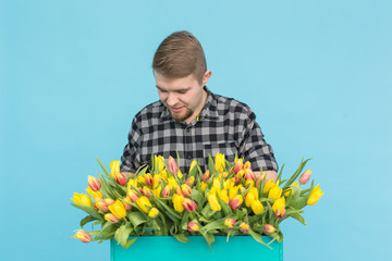 Handsome caucasian male gardener making a bouquet of tulips in blue studio.