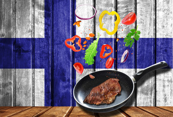 Fresh vegetables falling into the pan with meat, cooking concept on wooden flag background of Finland