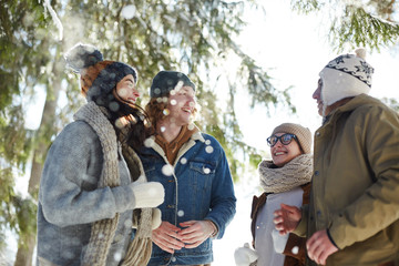Group of carefree  young people enjoying walk in beautiful winter forest lit by sunlight on  vacation