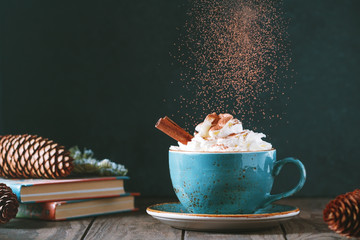 Hot chocolate with cream and cinnamon stick in a blue ceramic cup on a table with a books. The concept of winter or fall time. - 229318858