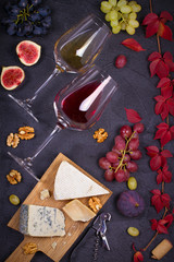 Fototapeta na wymiar Glass and bottle of wine with cheese, grapes, figs and nuts on black stone texture background. Wine and food. View from above, top studio shot