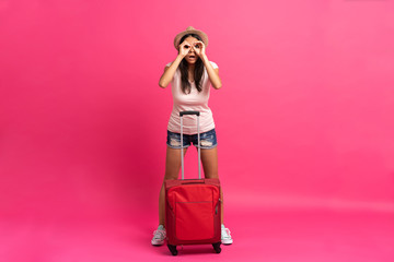Woman traveler with suitcase on color background.