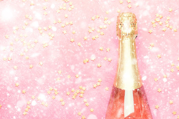 Christmas or New Year pink background with  bottle of sparkling wine, rose champagne and gold decor, top view