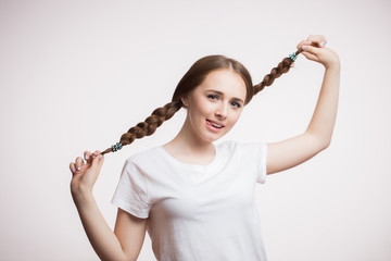 Cheerful young student or teen girl shows tongue and holds hands pigtails, smiles and looks at camera on white background