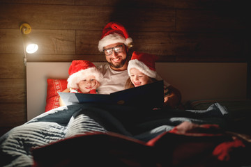 Merry Christmas! family father reads to children book before bed in bed