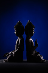Two Buddha Shakyamuni's figure in a meditation pose - vitarka mudra. The old statue brown color made of metal on a dark background.
