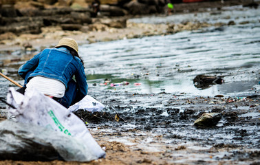 Volunteers sit and picking up garbage on the beach. Cleaner collecting garbage on the sea beach in...
