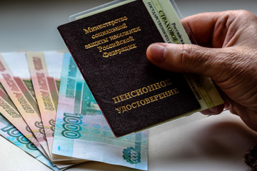 Woman's hand holding russian pension certificate, russian rubles in background. Russian translation - Ministry of Social Protection of Population of Russian Federation. Pension Certificate.