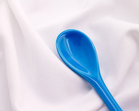 Blue ceramics spoon on white fabric background. Colorful concept.