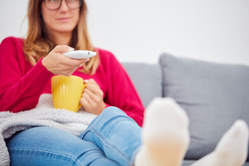 Girl holding TV remote and drinking coffee / tea on a couch.