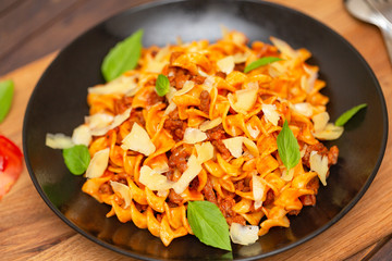 The Pasta Bolognese. Tagliatelle with minced meat, tomato sauce, Basil and Parmesan on a black plate on a dark wooden background.