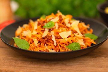 The Pasta Bolognese. Tagliatelle with minced meat, tomato sauce, Basil and Parmesan on a black plate on a dark wooden background.