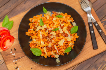 The Pasta Bolognese. Tagliatelle with minced meat, tomato sauce, Basil and Parmesan on a black plate on a dark wooden background.