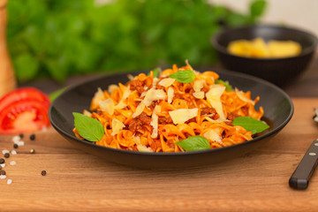 The Pasta Bolognese. Tagliatelle with minced meat, tomato sauce, Basil and Parmesan on a black plate on a dark wooden background.