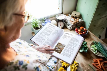Crédence de cuisine en verre imprimé Cuisinier Happy elderly woman reading a cookbook
