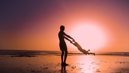 Ultra slow motion - silhouette of father and son playing together in the beach at sunset