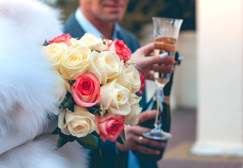 Wedding glasses with champagne in the hands of the newlyweds next to a wedding bouquet of white and...