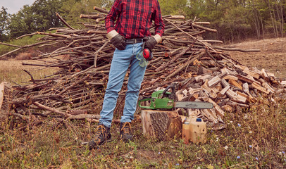 Lumberjack with chainsaw and pile of cut woods.