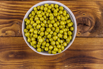 Bowl with canned green peas  on wooden table. Top view