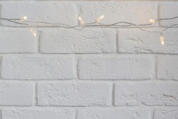Christmas lights on the white brick wall background with copy space.