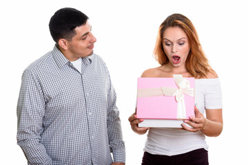 Young Hispanic couple in love with woman opening gift box looking surprised