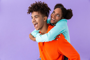 Obraz premium Photo of pleased african american man piggybacking his teenage sister, isolated over violet background
