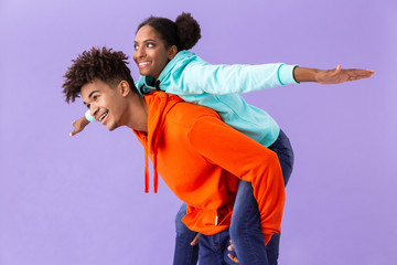 Obraz premium Photo of beautiful african american guy piggybacking his girlfriend, isolated over violet background