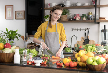 Healthy young woman in a kitchen preparing fruits and vegetables for healthy meal and salad