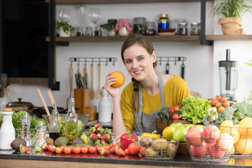 Healthy young woman in a kitchen preparing fruits and vegetables for healthy meal and salad