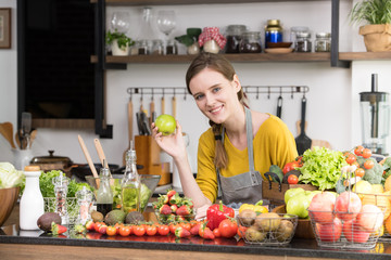Healthy young woman in a kitchen preparing fruits and vegetables for healthy meal and salad