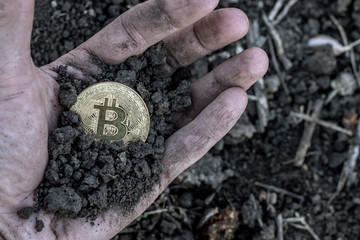 male miner's hand on the palm of the hand with the ground holding a gold coin bitcoin on the background of black earth