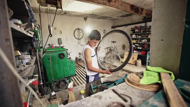 Young poor boy repairs his bike in an old studio.