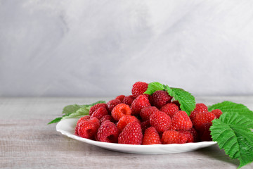  Red fresh raspberries on white rustic wood background. Plate with natural ripe organic berries with green leaves.flat lay with copy space