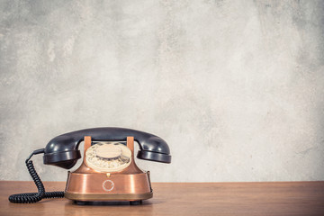 Retro antique classic outdated copper with black color rotary telephone from circa 1950s on wooden...