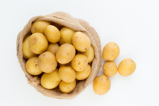 Sack of fresh raw potatoes on wooden background, top view