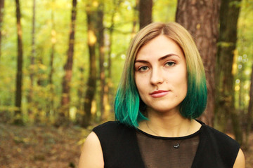 The blonde girl with blue ends in a black dress stands in the woods and reads a book. The sun is warm and the sun is in the air. A portrait in the woods. Natural background. The woman is a witch
