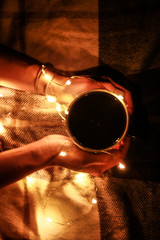 Home atmosphere. Cosiness. Warm colors. A mug of tea in the hands of the girl is enlightened with...
