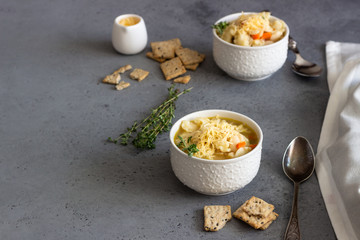 Two white bowls of Italian soup minestrone with pasta and white beans topped with fresh thyme and served with crackers on grey concrete background. Vegetarian food concept.