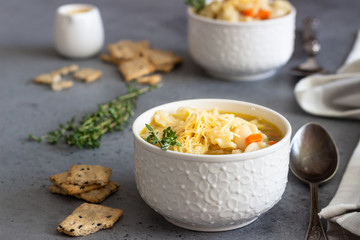 Two white bowls of Italian soup minestrone with pasta and white beans topped with fresh thyme and served with crackers on grey concrete background. Vegetarian food concept.