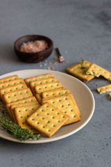 Thin crispy salted crackers with seeds and herbs on grey concrete background. 