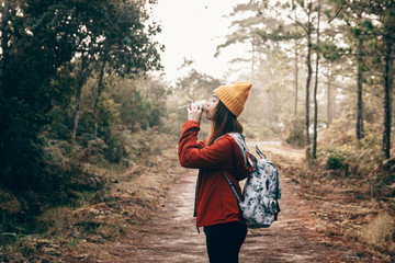 Traveler girl wear yellow knit hat, with backpack, drinking hot coffee in the forest. Warm tone preset.