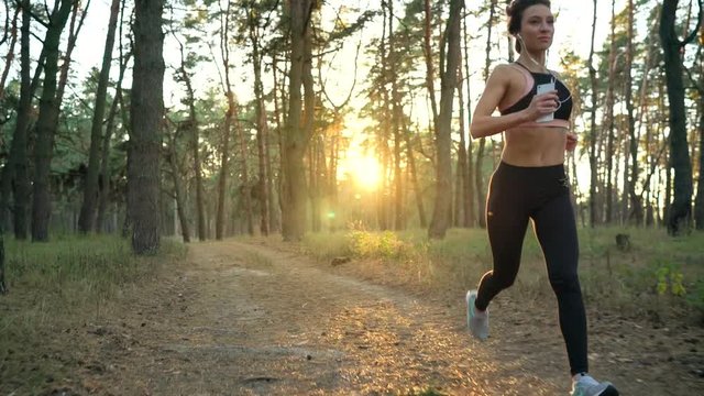 Close up of woman with headphones running through an autumn forest at sunset. Slow motion