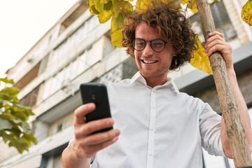 Bottom view of businessman standing outdoors and using smartphone and free wireless. Smiling man...