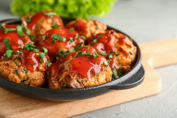 Frying pan with tasty sausage balls and tomato sauce on wooden board, closeup