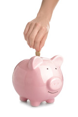Woman putting coin into piggy bank on white background