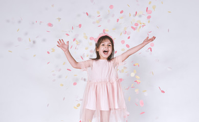 Funny cute little girl wearing pink dress in tulle with princess crown on head isolated on white background rise hands up enjoy confetti. Pretty little girl celebrating her birthday party, having fun