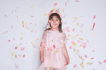 Studio portrtait of cute little girl wearing pink dress in tulle with princess crown on head isolated on white background enjoy confetti. Happy smiling girl celebrating her birthday party, having fun